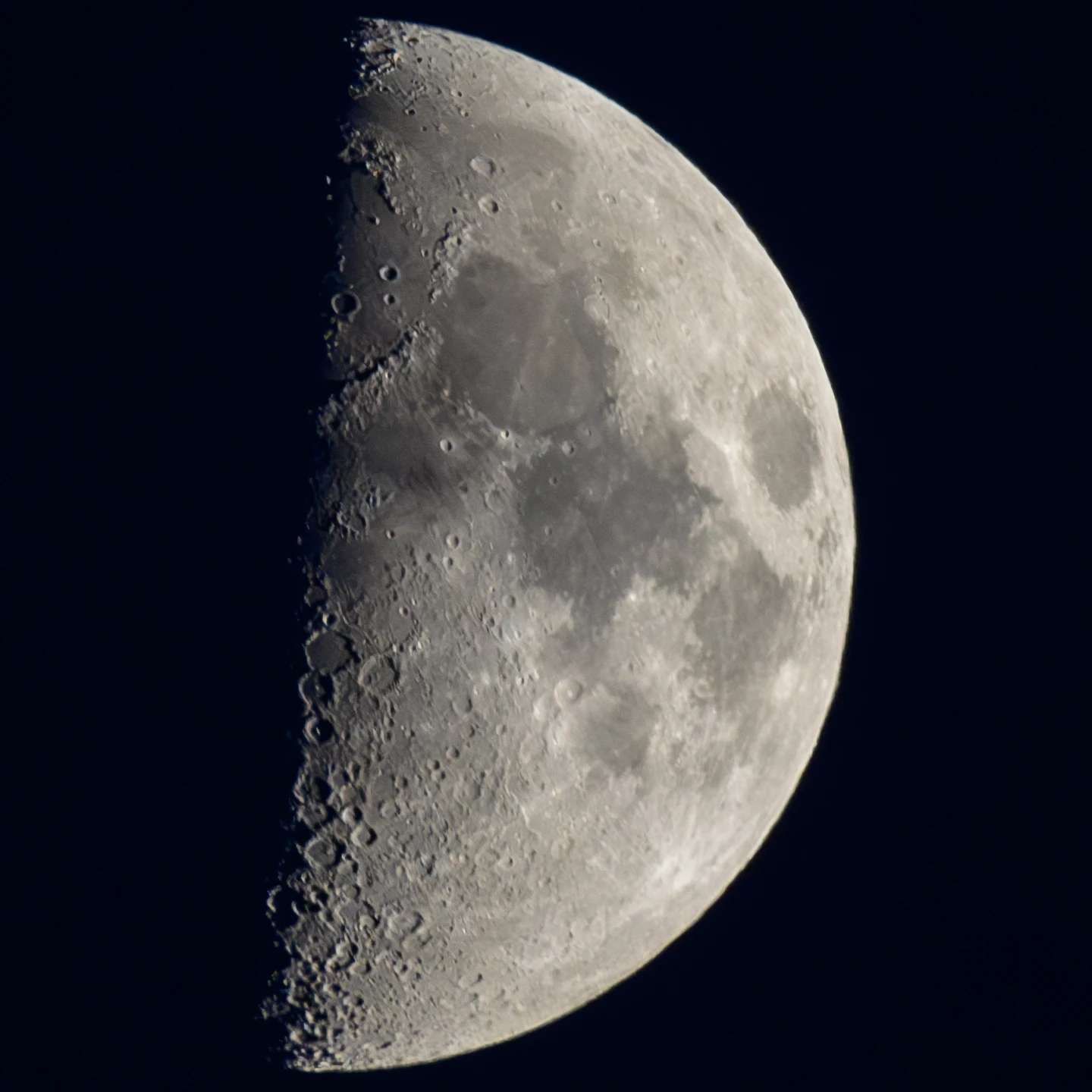 Photo of the surface of the moon, as seen from earth. Half of the moon is visible, covered in craters and mare.