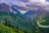 Color photo. The valley of McDonald Creek, in Glacier National Park, leads up along the right of the frame. Above it a partial rainbow is visible, catching sunlight emerging through a gap in the dark clouds above. Mount Cannon rises, rocky and dramatic, on the left of the frame.