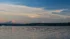 Color photo. Sunset, with the snowy peak of Mount Rainier turning red. Above, in a darkening blue sky, are wispy clouds stretching across the frame. Below, houses dot the dark shore of Lake Washington, its waters occupying the lower third of the photo.